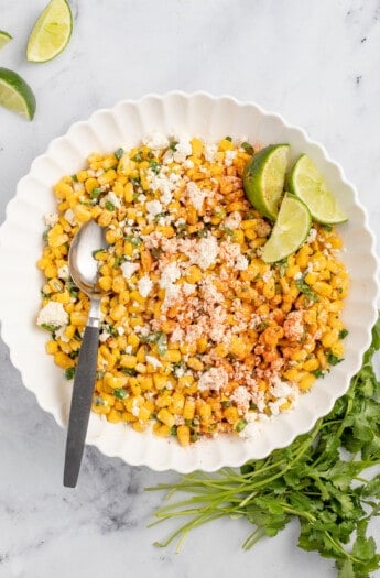 Mexican street corn in a bowl with lime wedges on the side.