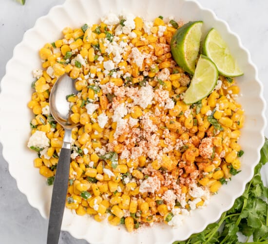 Mexican street corn in a bowl with lime wedges on the side.