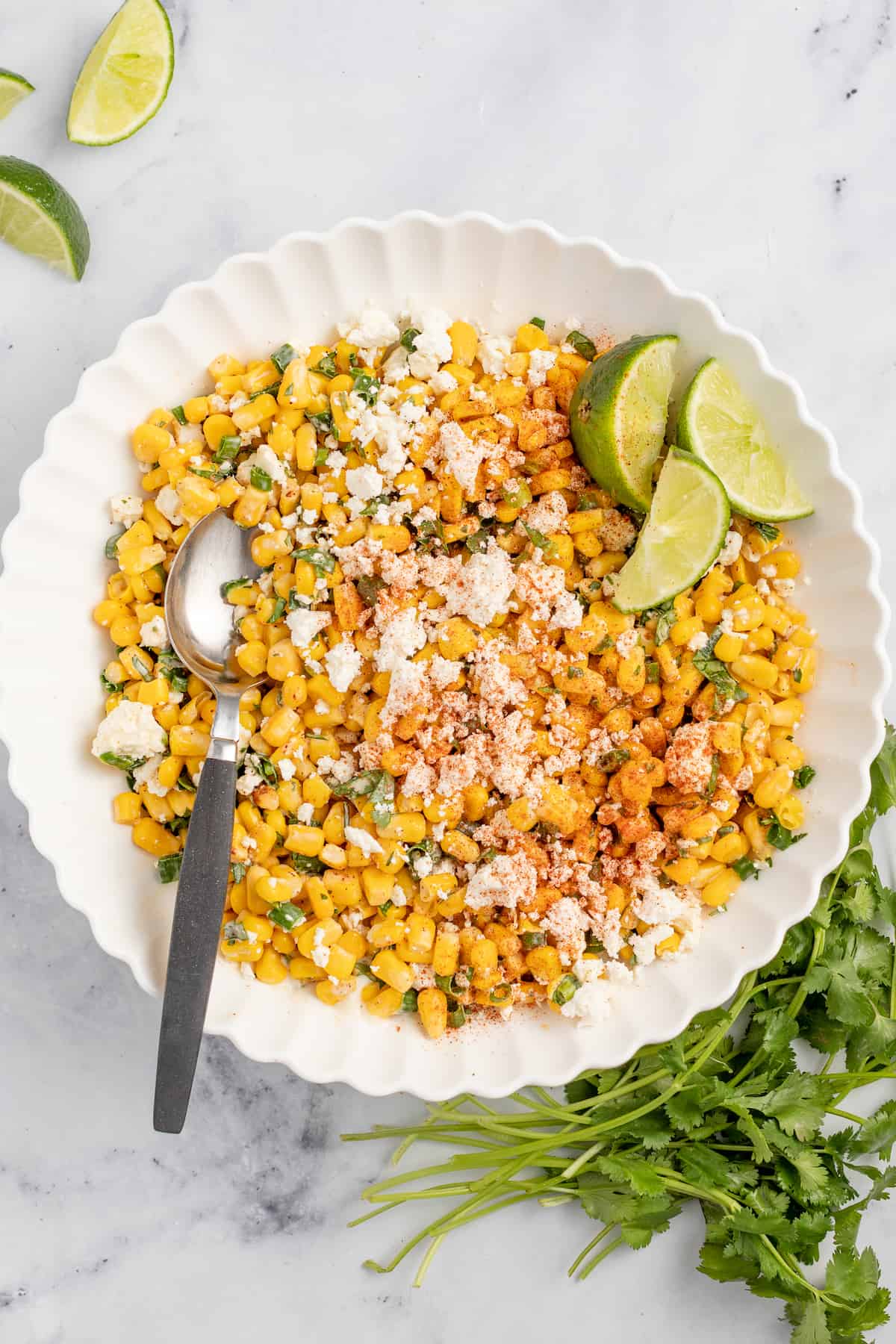 Mexican street corn in a bowl with lime wedges on the side.