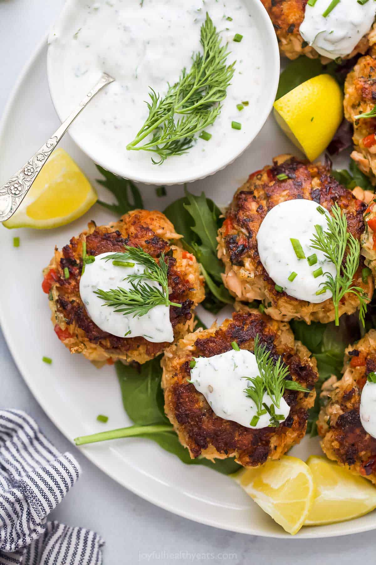 Side-shot of salmon cakes with dill sauce on the side. 