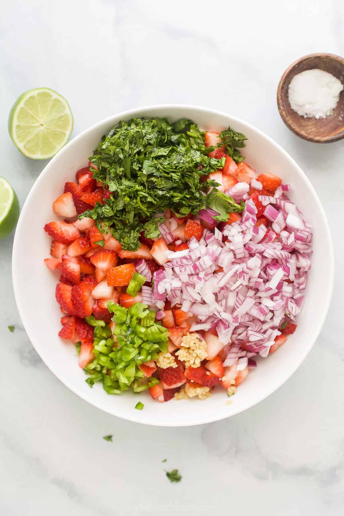 This 10-minute strawberry salsa is fruity, spicy, and tangy all in one bite. It's the perfect summer appetizer with corn chips! Adding the ingredients to a mixing bowl.