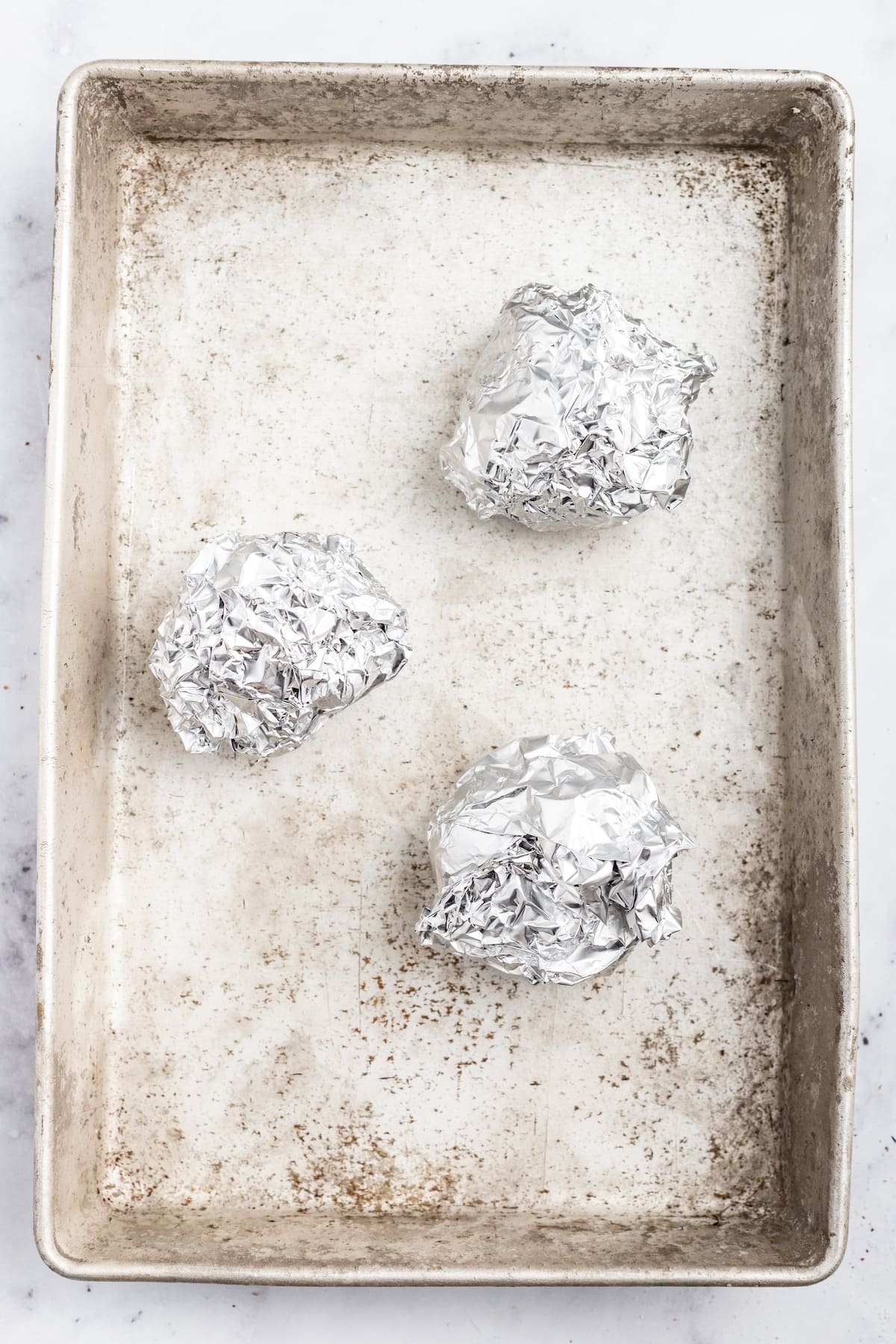 Garlic bulbs wrapped in foil on a baking sheet. 