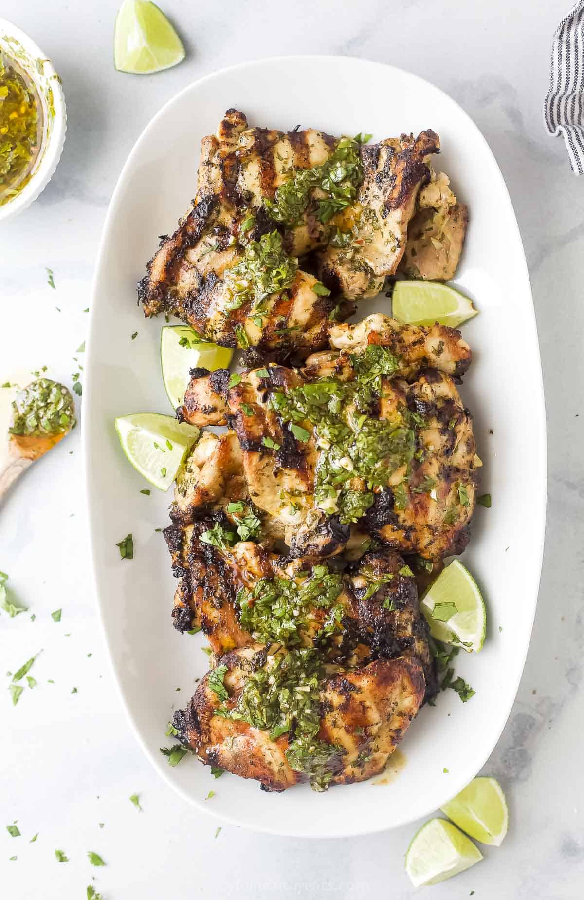 Topped with extra chimichurri, this juicy chimichurri chicken will be your new excuse to fire up the grill this summer. You'll love it! Chimichurri chicken with grill marks on a plate.
