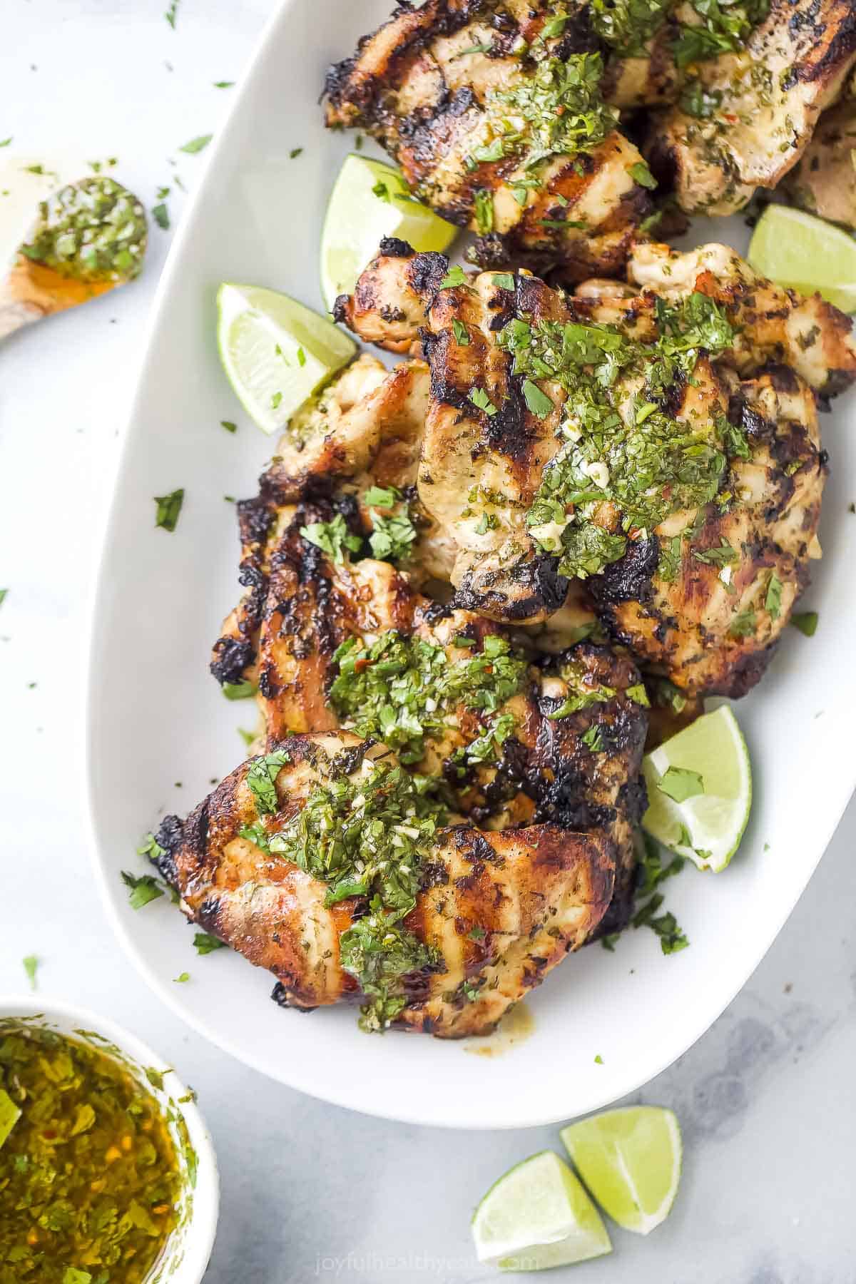 Topped with extra chimichurri, this juicy chimichurri chicken will be your new excuse to fire up the grill this summer. You'll love it! Angled shot of grilled chimichurri thighs on a plate.