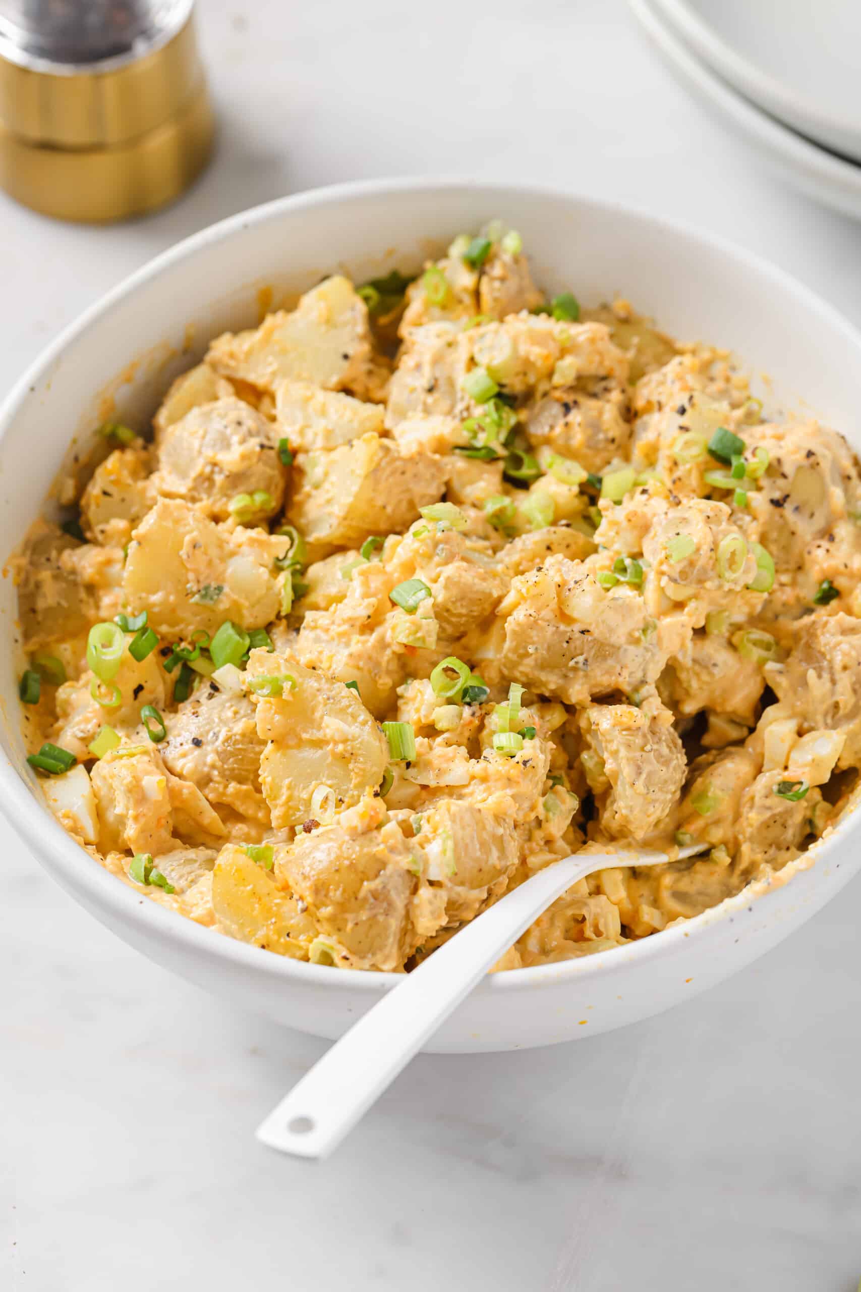 Bowl of deviled egg potato salad with green onions. 