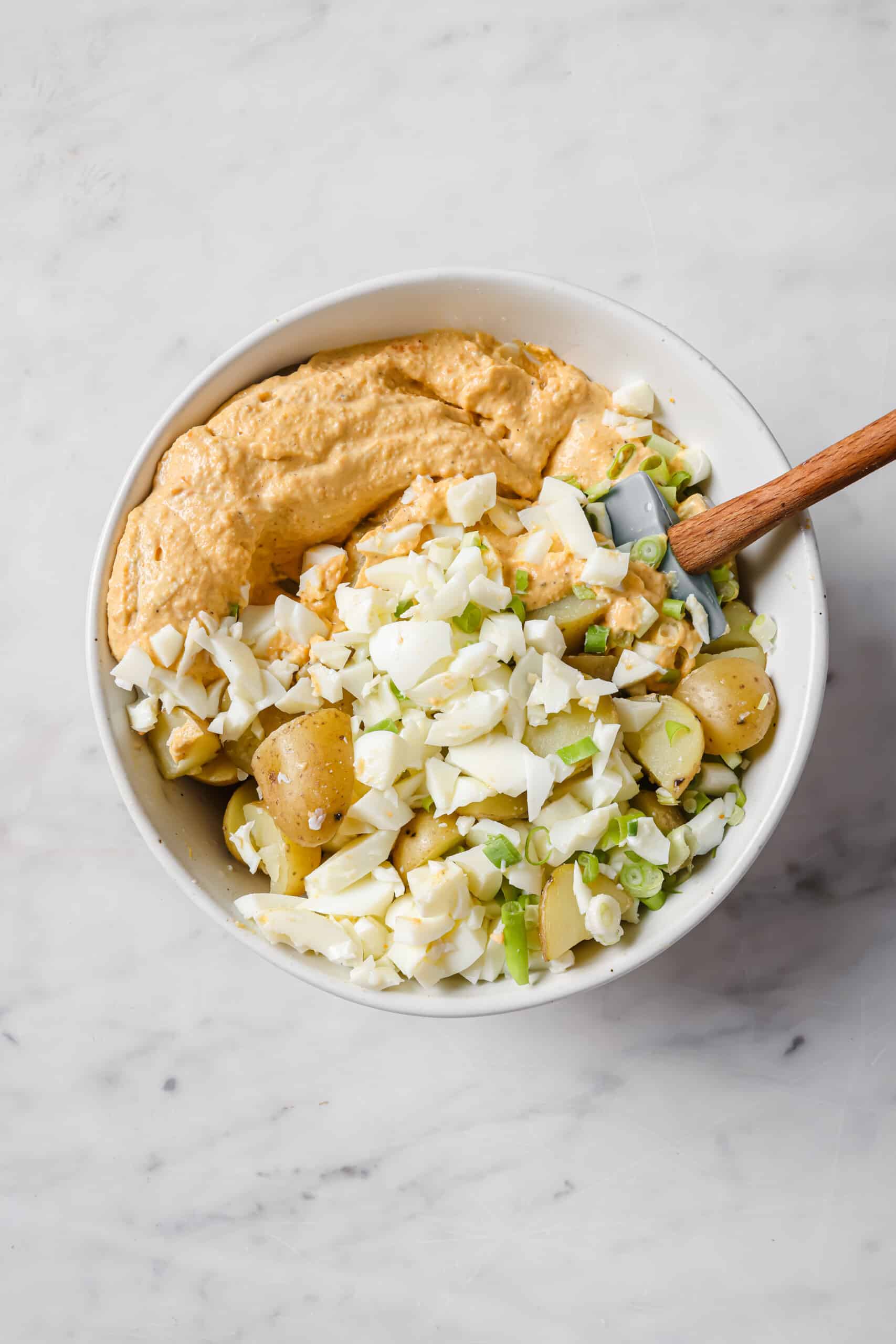 Mixing the sauce, potatoes, eggs, and green onion.