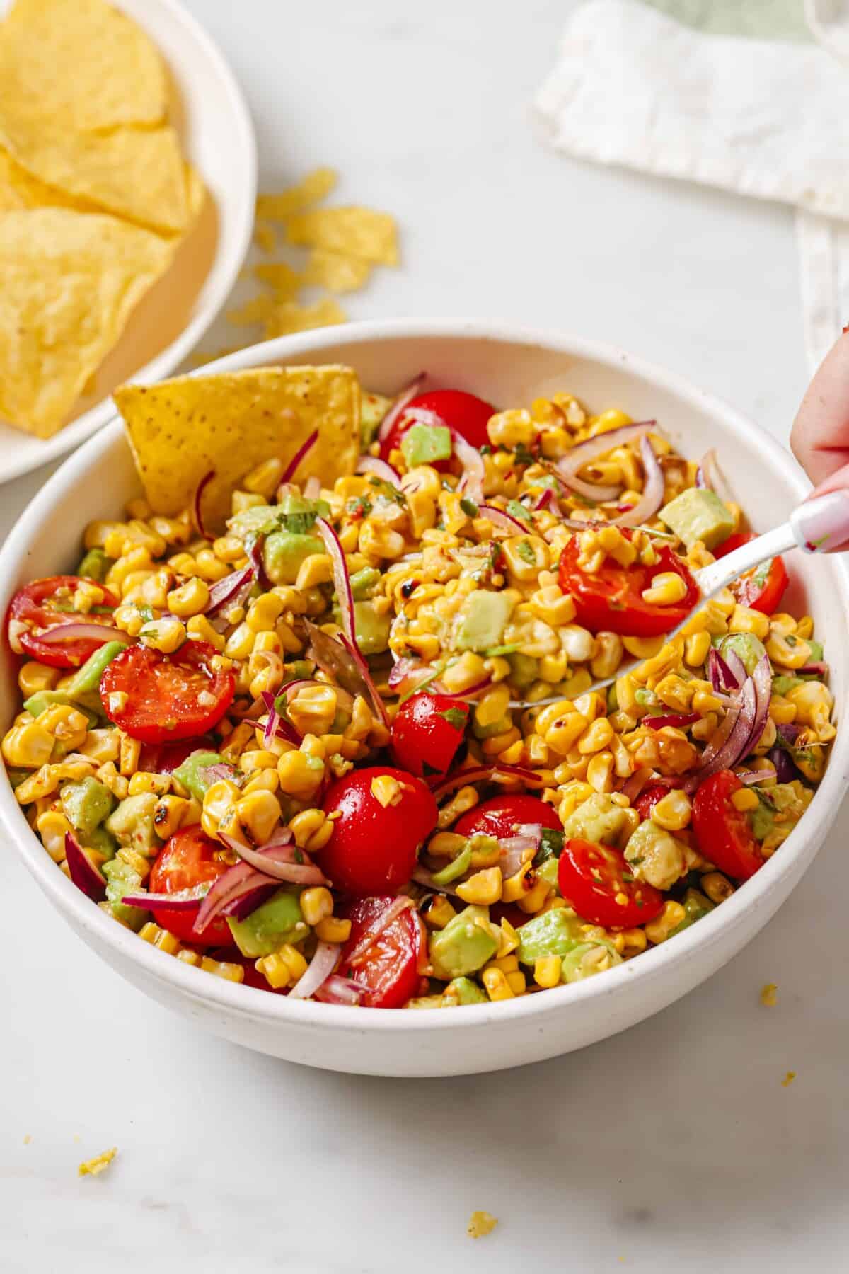 Bowl of avocado corn salad with corn chips.
