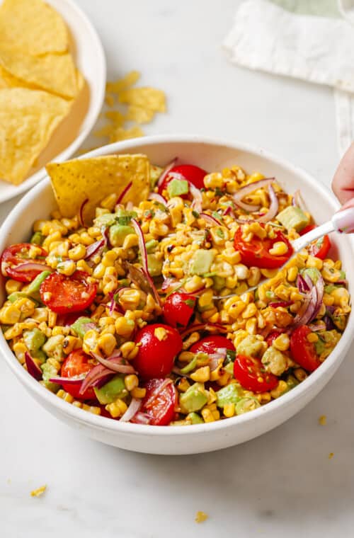 Bowl of avocado corn salad with corn chips.