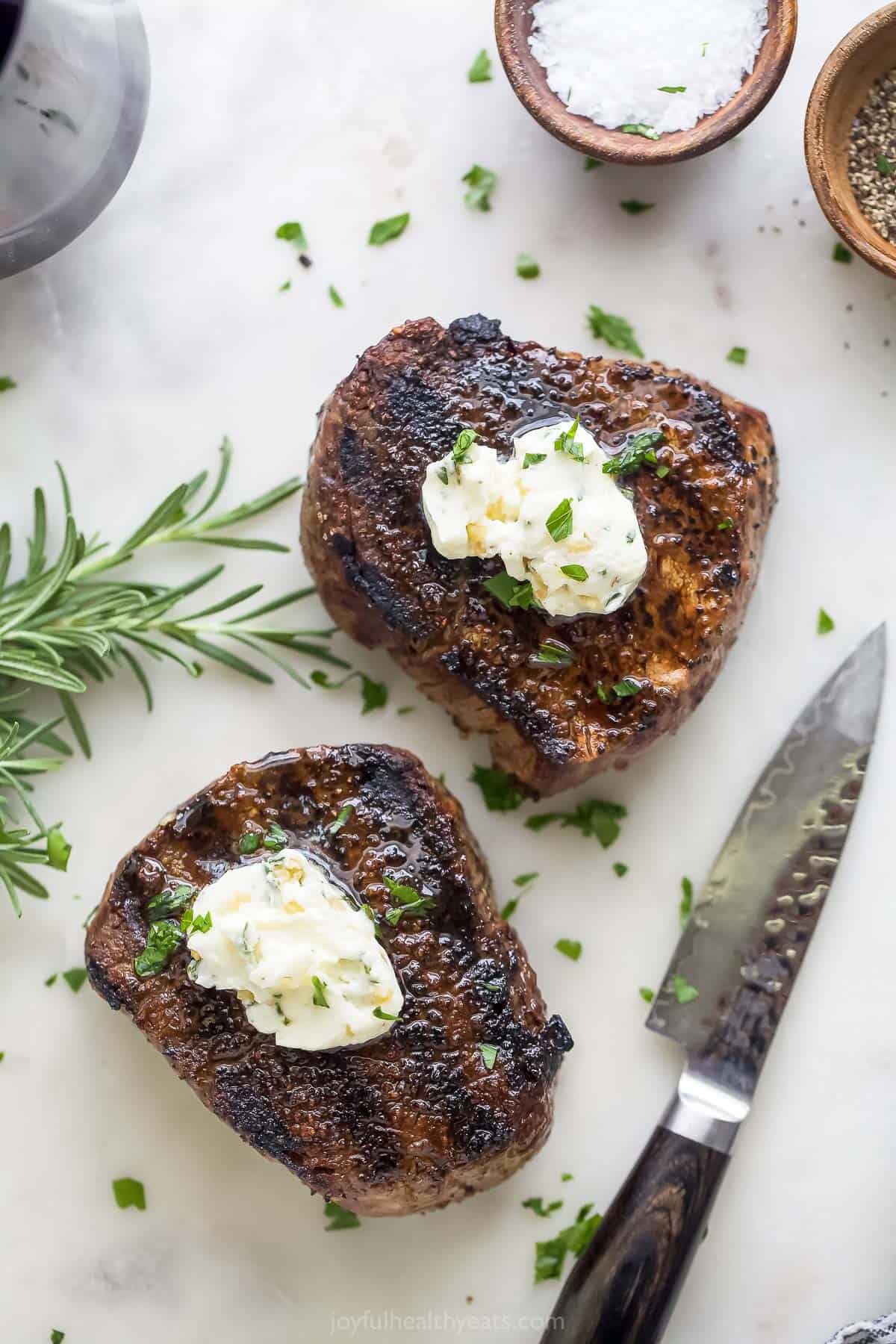 Two filet mignons with knobs of butter on top.