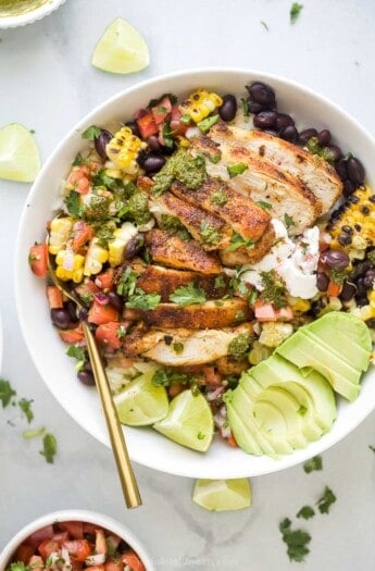 Chicken burrito bowl with avocado, lime wedges, and other toppings.