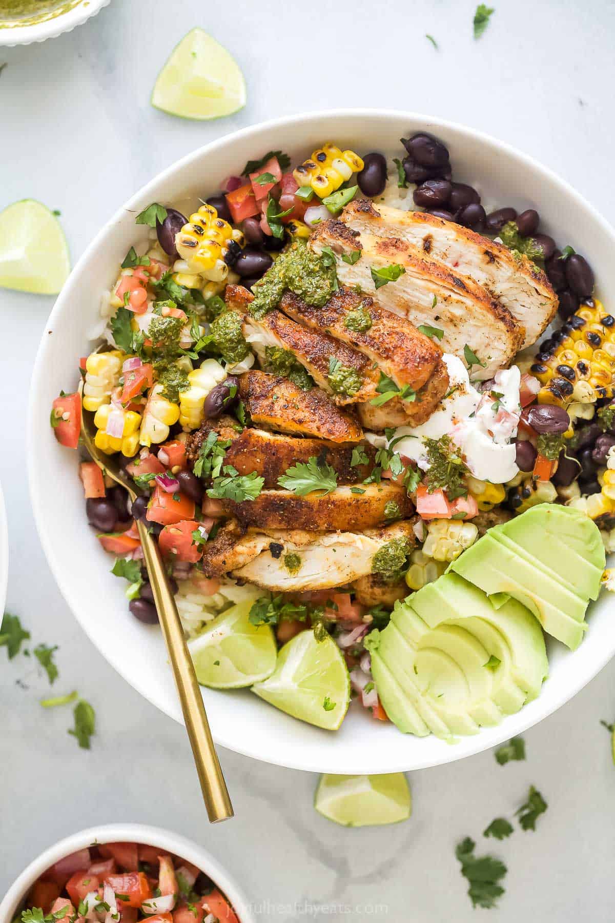 Chicken burrito bowl with avocado, lime wedges, and other toppings.