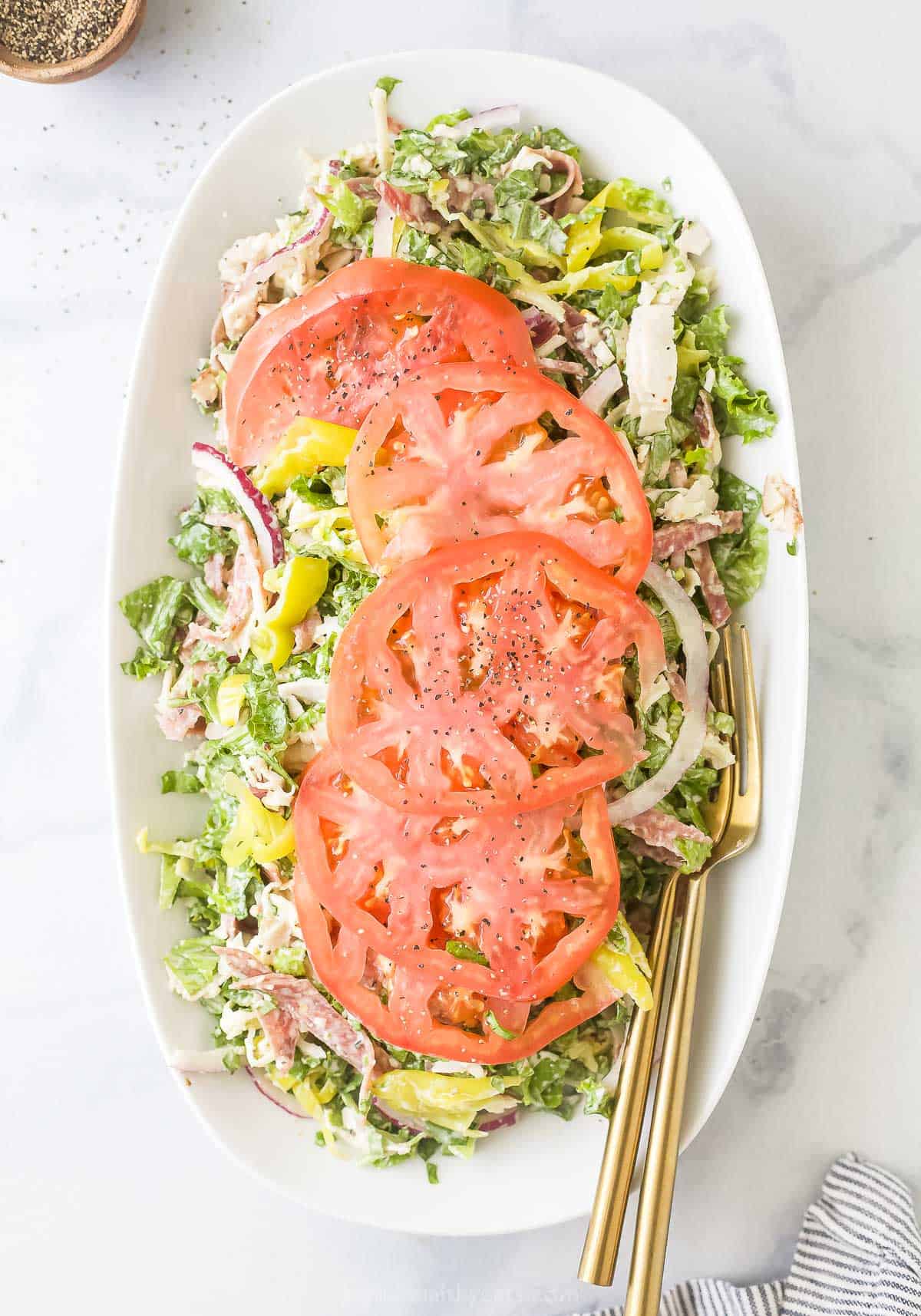 Plate of Italian grinder salad with large tomato slices on top. 