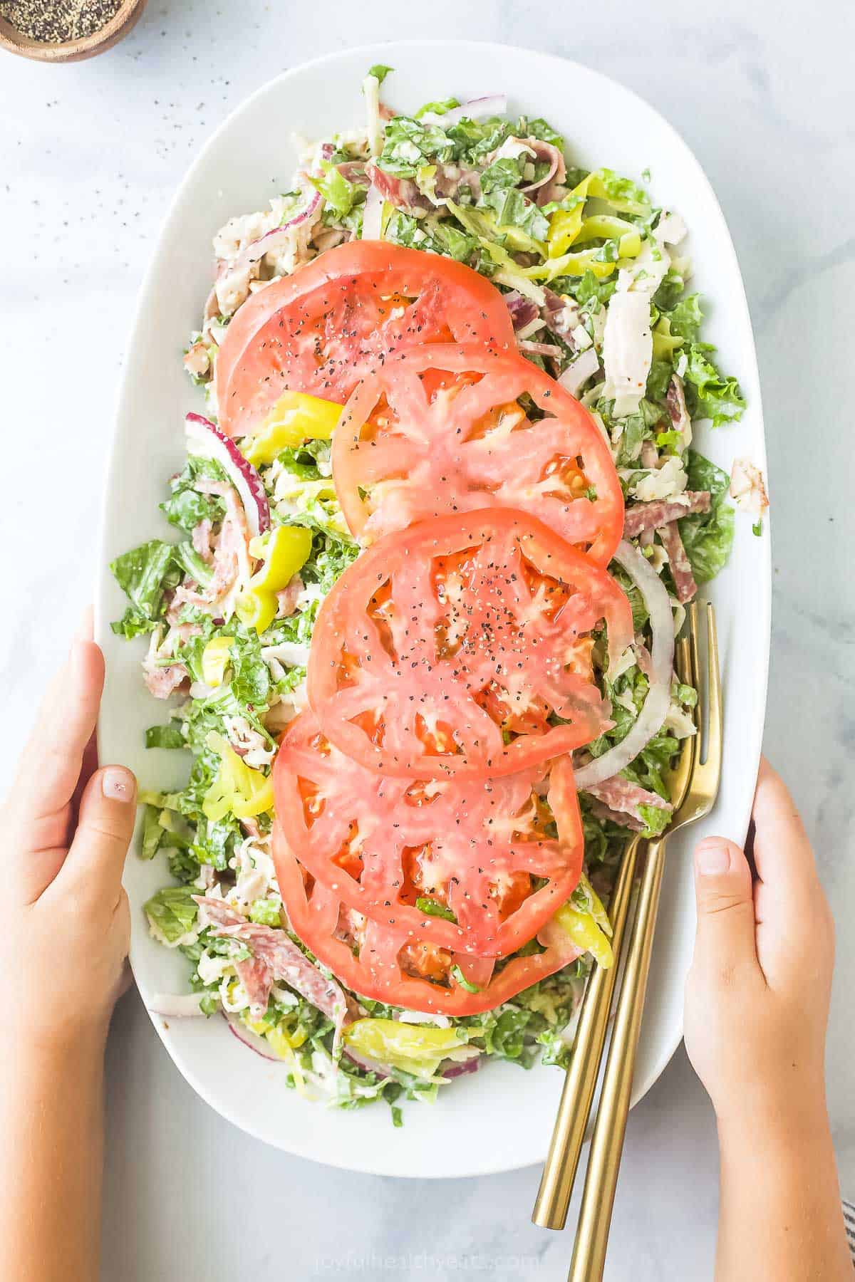 Grabbing the plate of Italian grinder salad recipe with sliced tomatoes on top. 