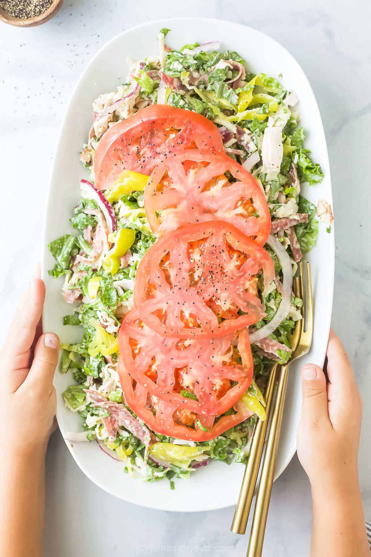 This easy Italian grinder salad recipe with homemade dressing is a trending 15-minute side that'll be a hit at the dinner table. Grabbing the plate of Italian grinder salad recipe with sliced tomatoes on top.