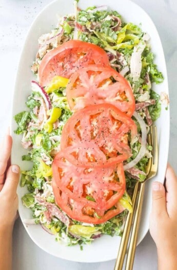 Grabbing the plate of Italian grinder salad recipe with sliced tomatoes on top.