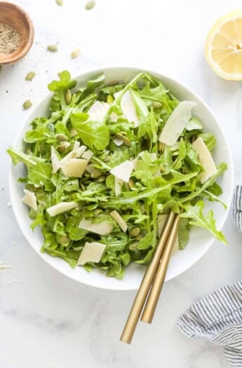 Bowl of arugula salad with shaved parmesan on top.