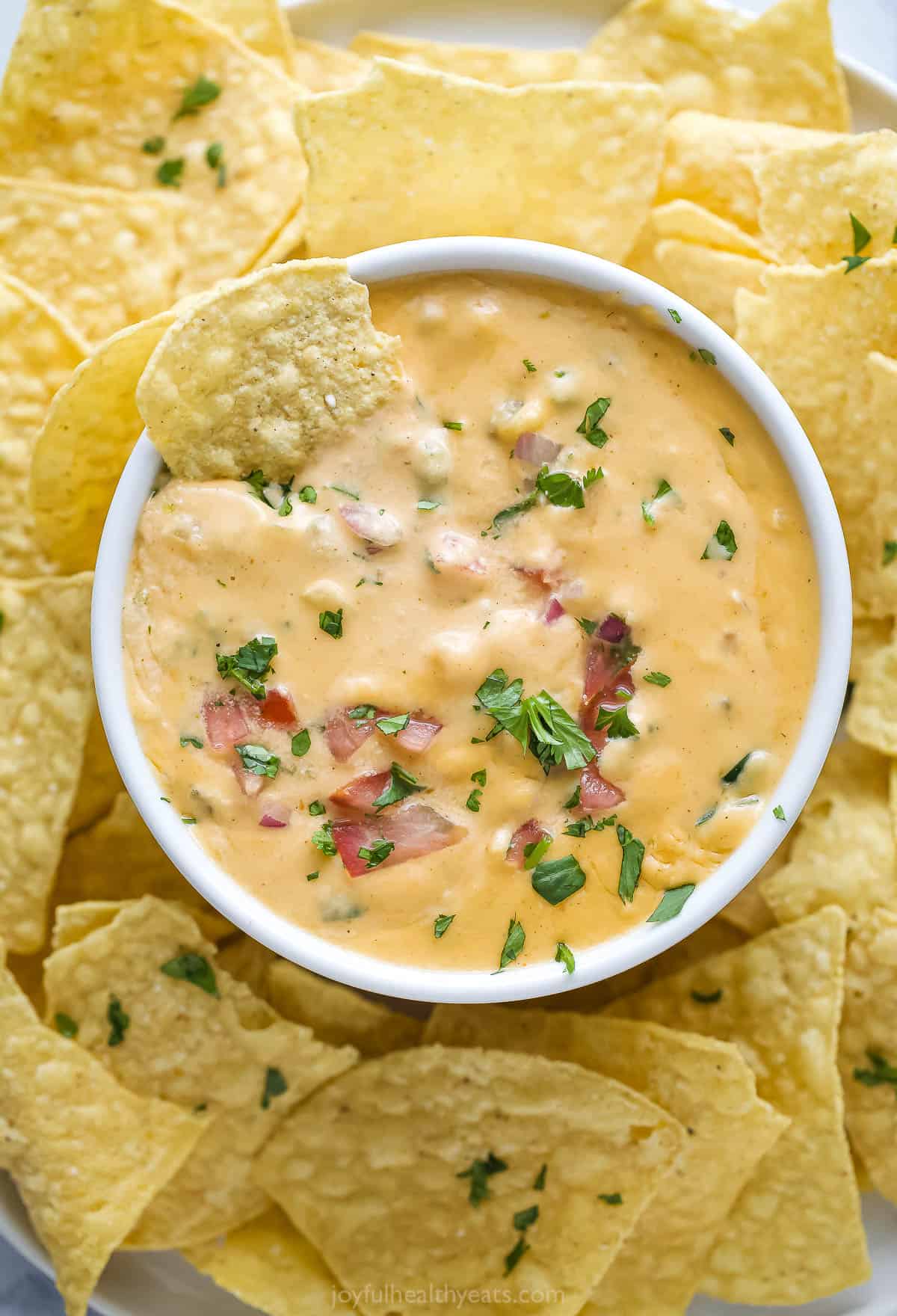 A corn chip in queso dip with pico de gallo. 