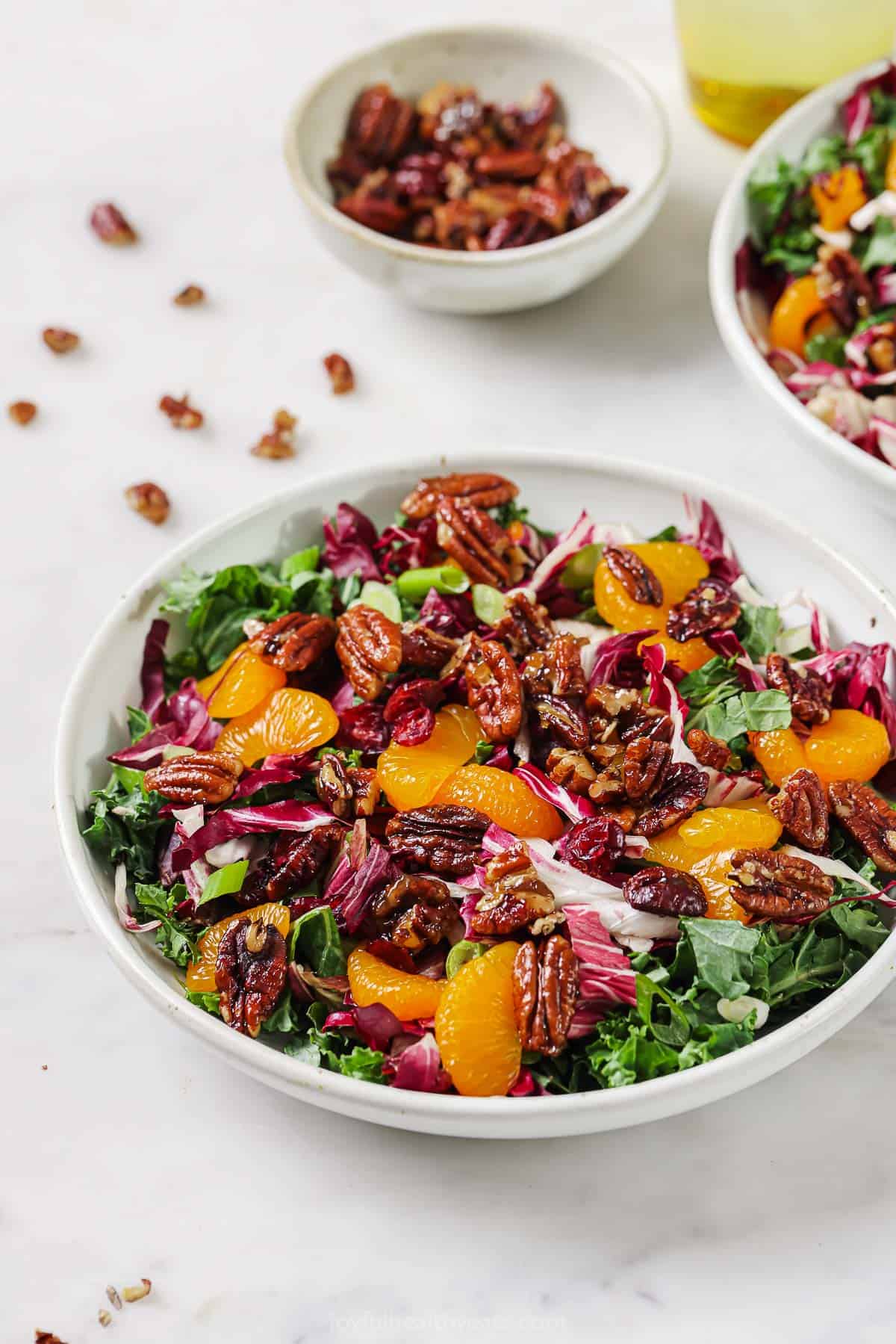 Bowl of kale salad with dressing and candied pecans.