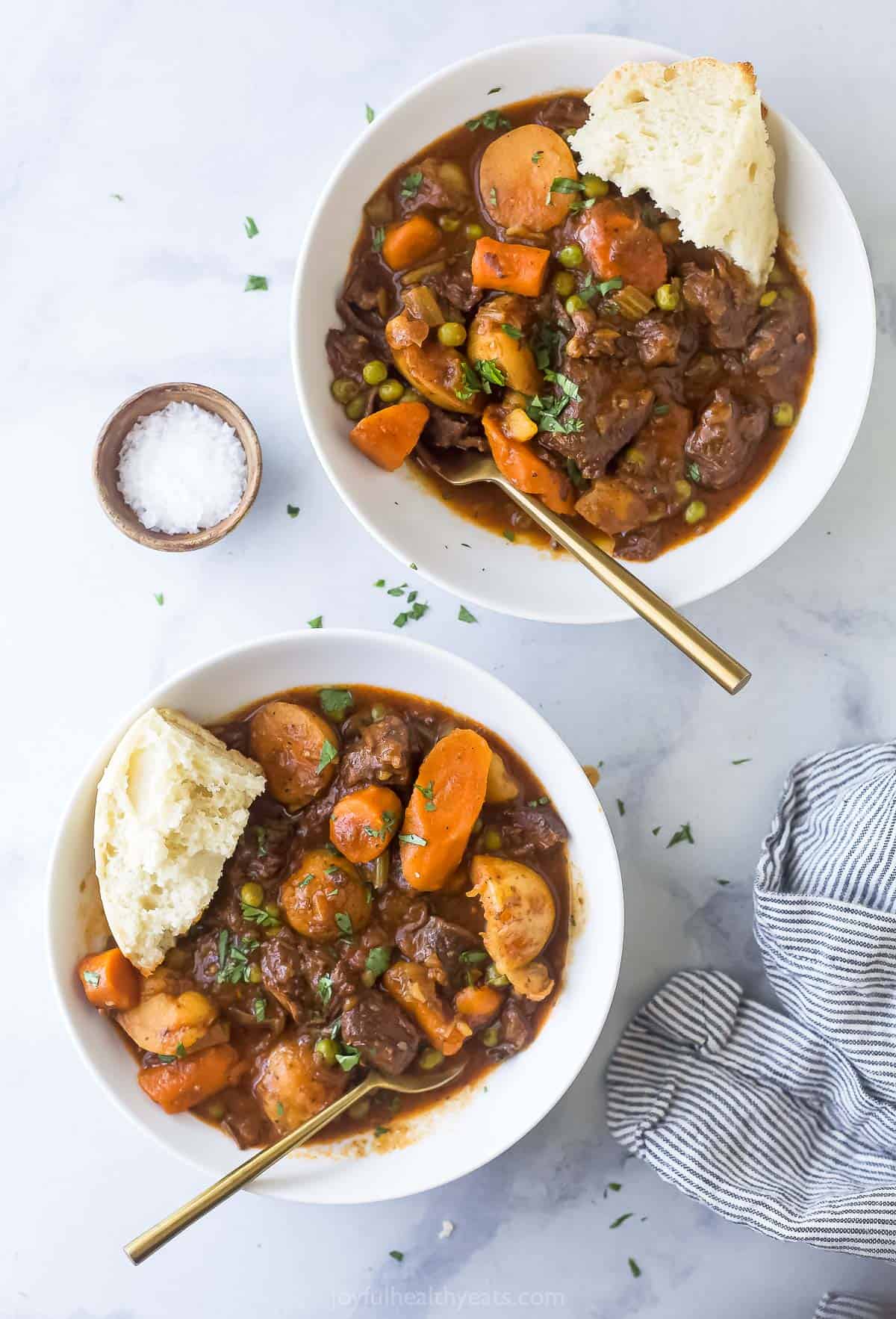 Two bowls of beef stew with bread. 