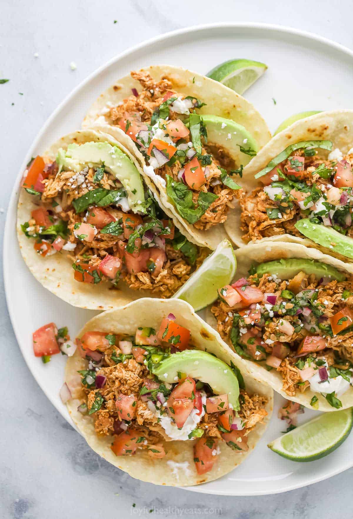 A plate of rotisserie chicken tacos with avocado and pico de gallo on top. 