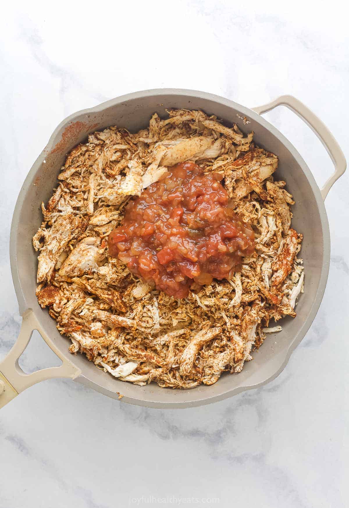 Adding the salsa and water to the seasoned chicken in the pan.