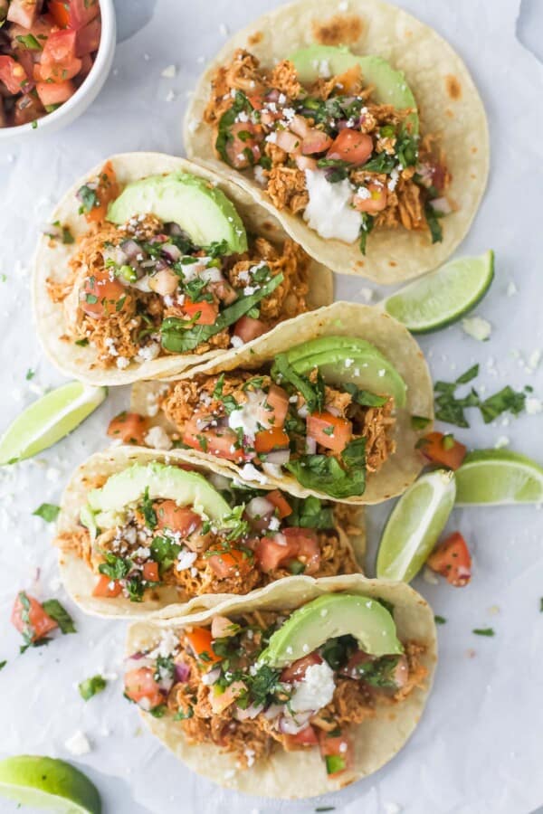 Several shredded chicken tacos with sliced avocado, queso fresco, and pico de gallo.