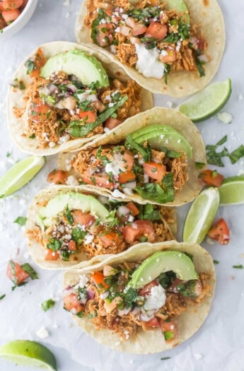 5 rotisserie chicken tacos with pico de gallo and sliced avocado on top.