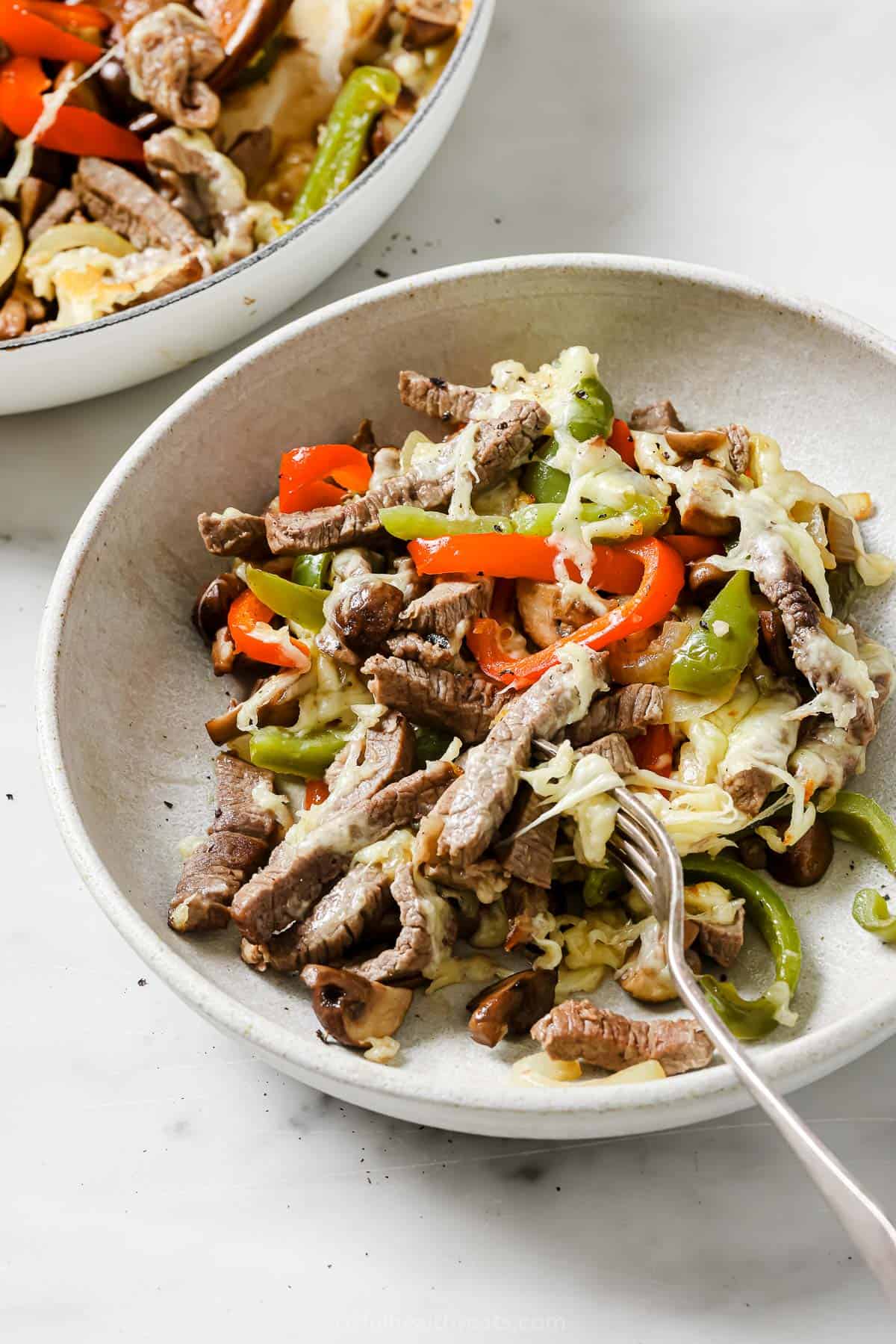 Philly cheesesteak skillet in a bowl with melty mozzarella on top. 