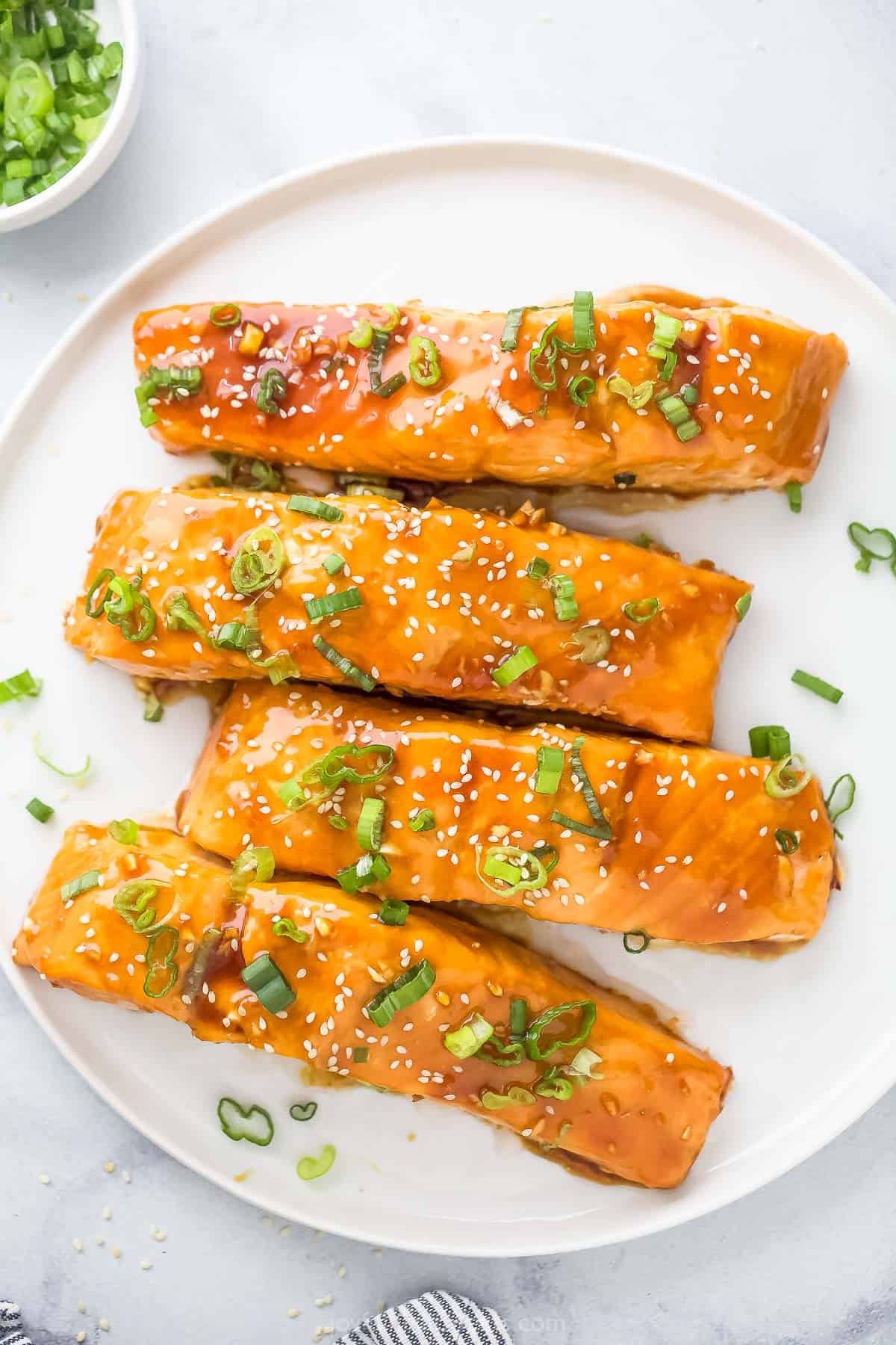 Teriyaki salmon with green onions and sesame seeds on a plate. 