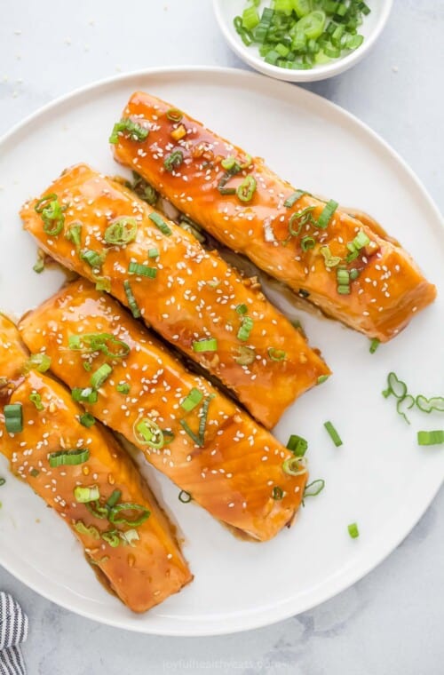 Plate of teriyaki salmon filets with green onions and sesame seeds.