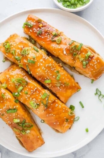 Plate of teriyaki salmon filets with green onions and sesame seeds.