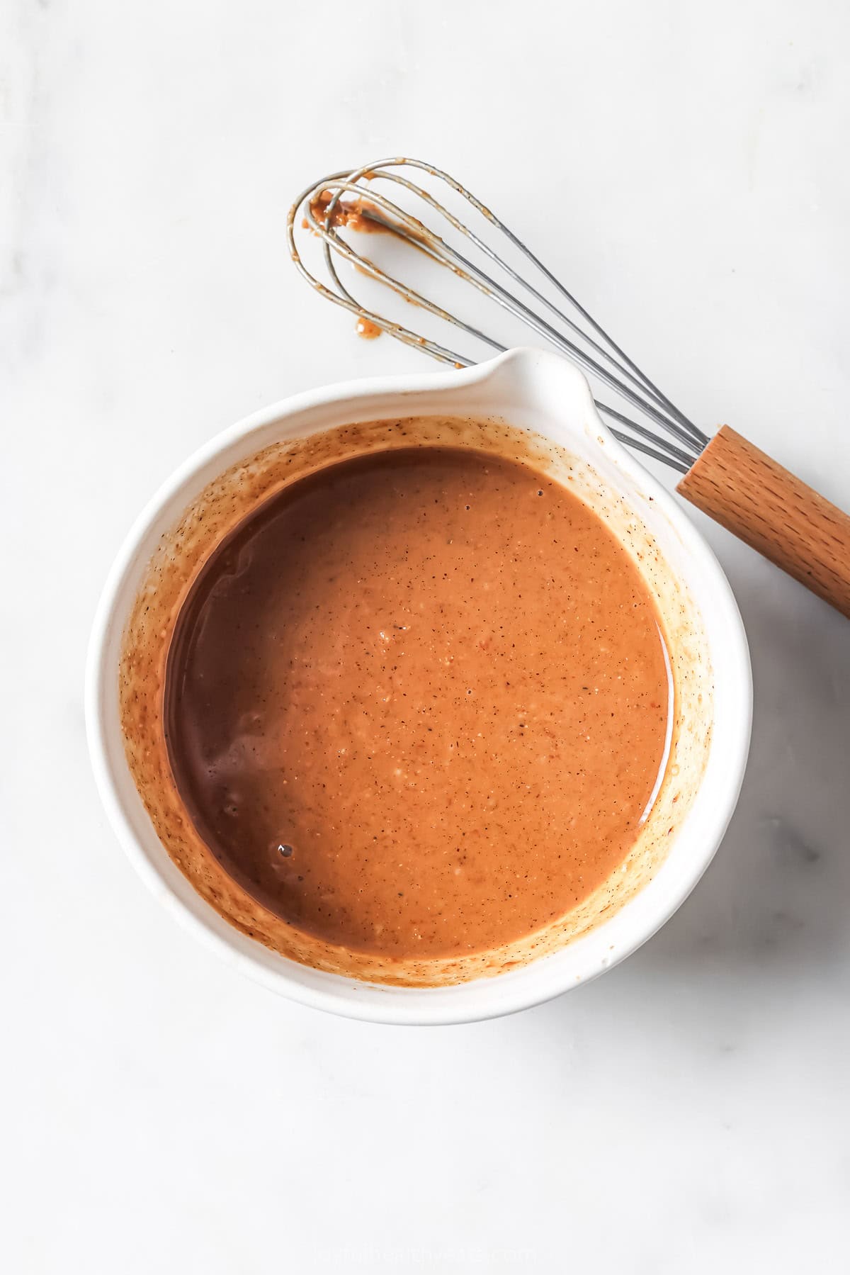 Overhead view of spicy peanut dressing in bowl with whisk