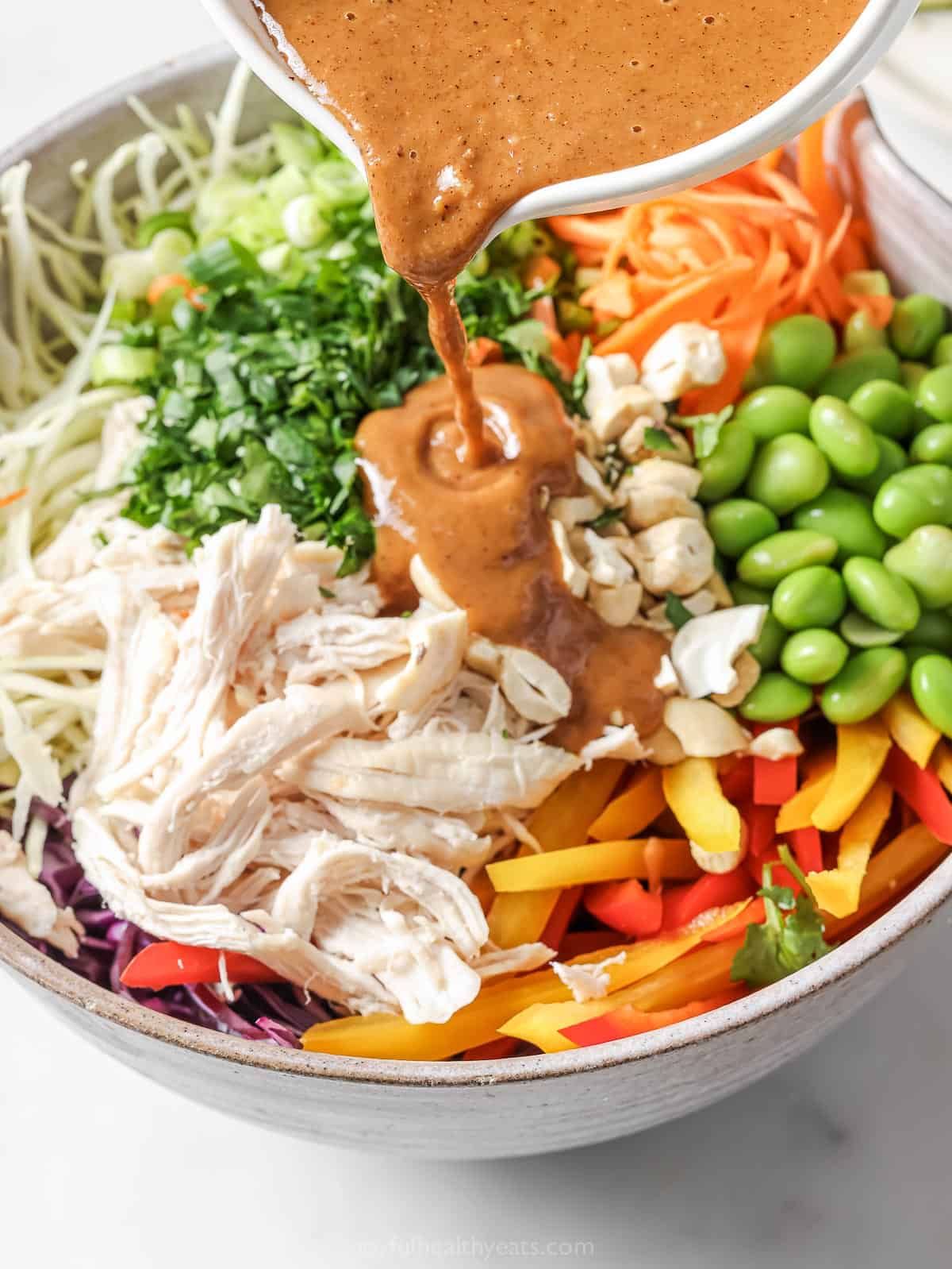 Pouring peanut dressing into ingredients for Thai salad