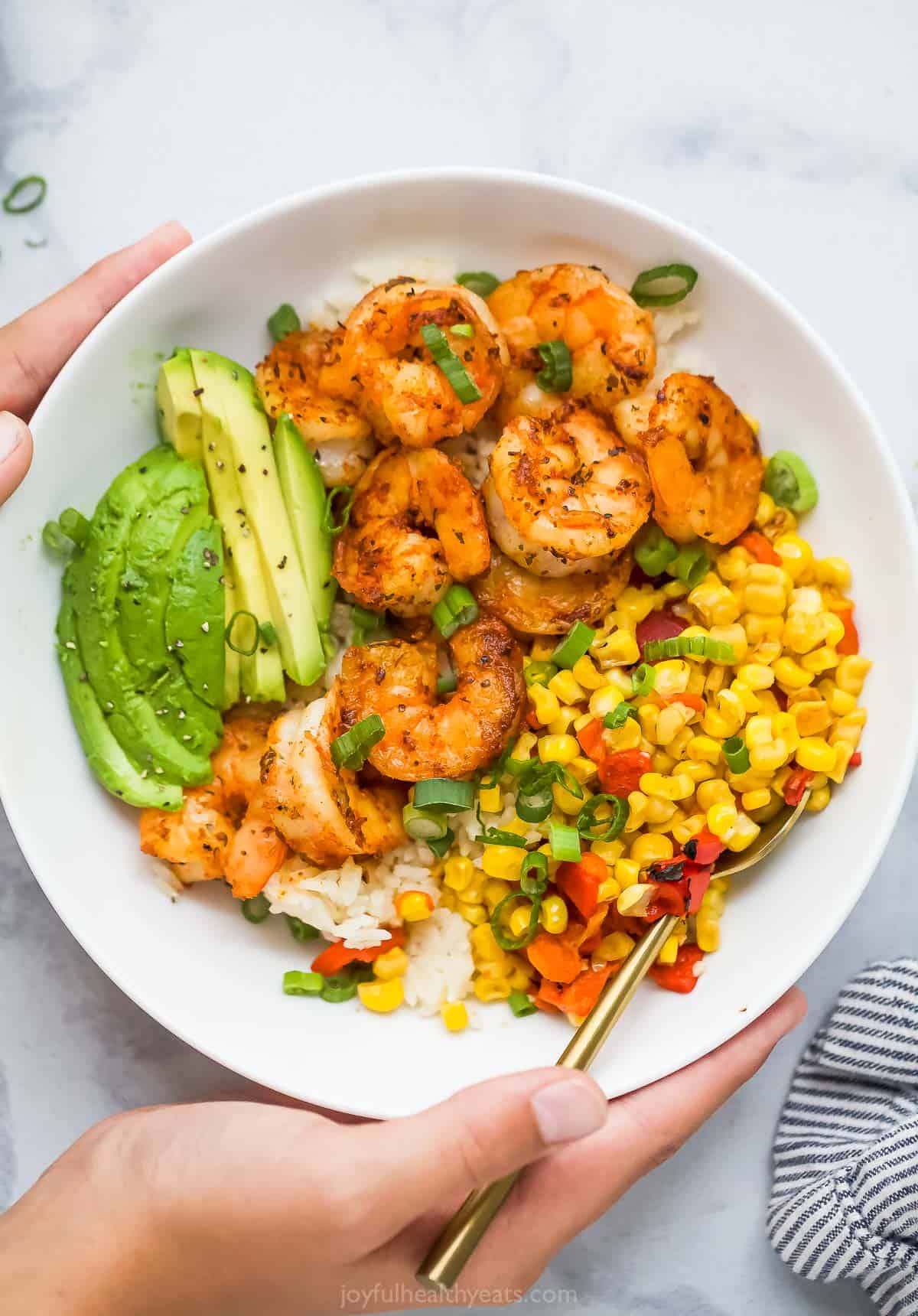 Hands holding blackened shrimp bowl with corn relish