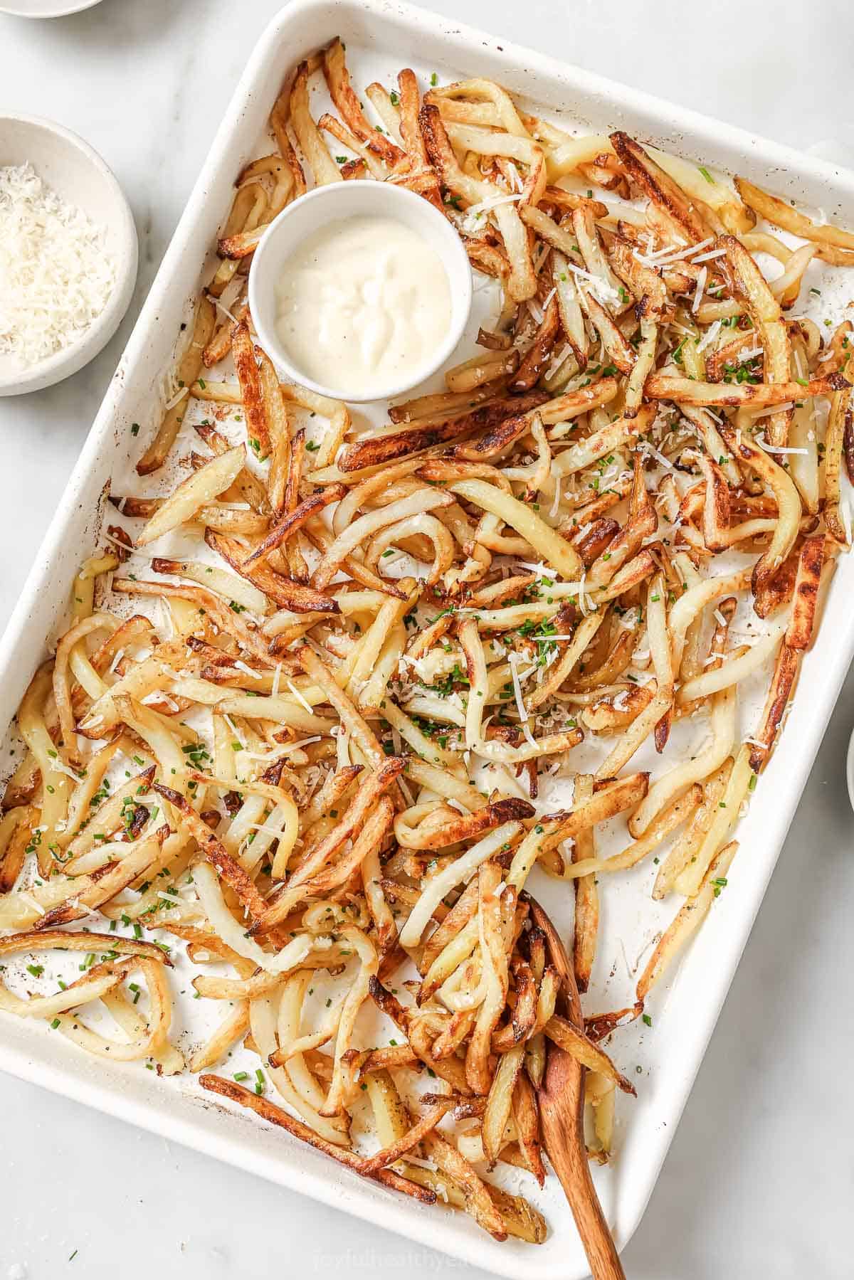 Cheesy Parmesan Truffle Fries are the perfect snack or party app when you’re feeling a little fancy. Baked in the oven and super crispy! Overhead view of Parmesan truffle fries on pan with bowl of aioli