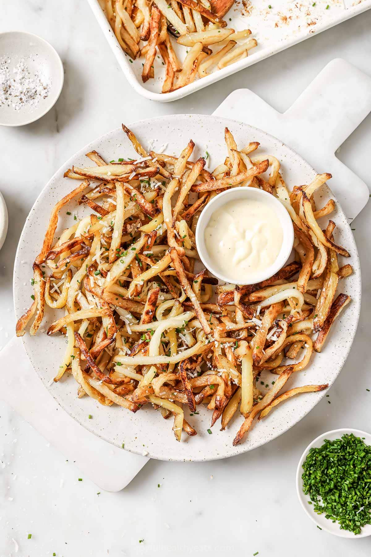 Cheesy Parmesan Truffle Fries are the perfect snack or party app when you’re feeling a little fancy. Baked in the oven and super crispy! Overhead view of Parmesan truffle fries on platter with bowl of aioli