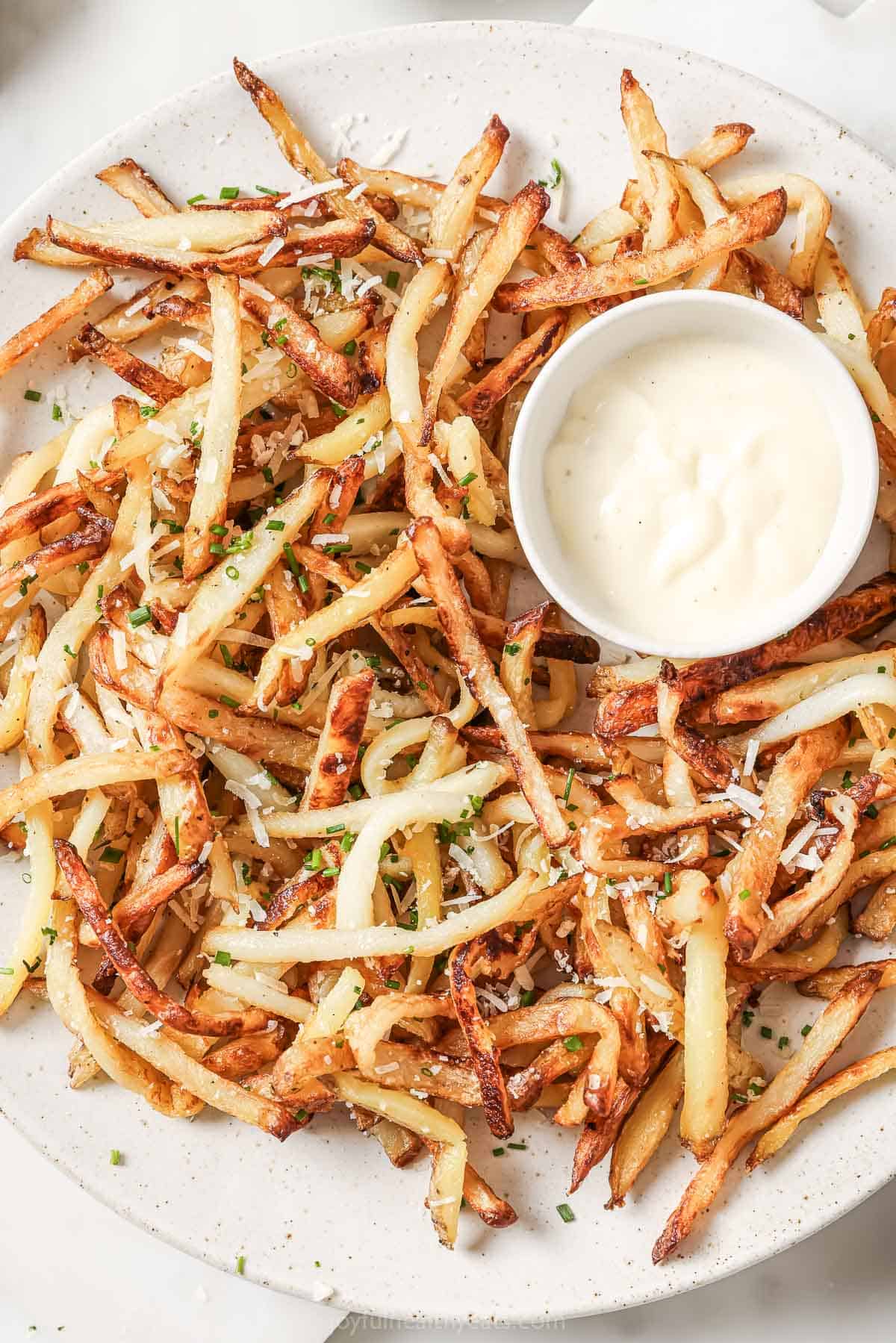 Cheesy Parmesan Truffle Fries are the perfect snack or party app when you’re feeling a little fancy. Baked in the oven and super crispy! Overhead view of Parmesan truffle fries on plate with small bowl of aioli