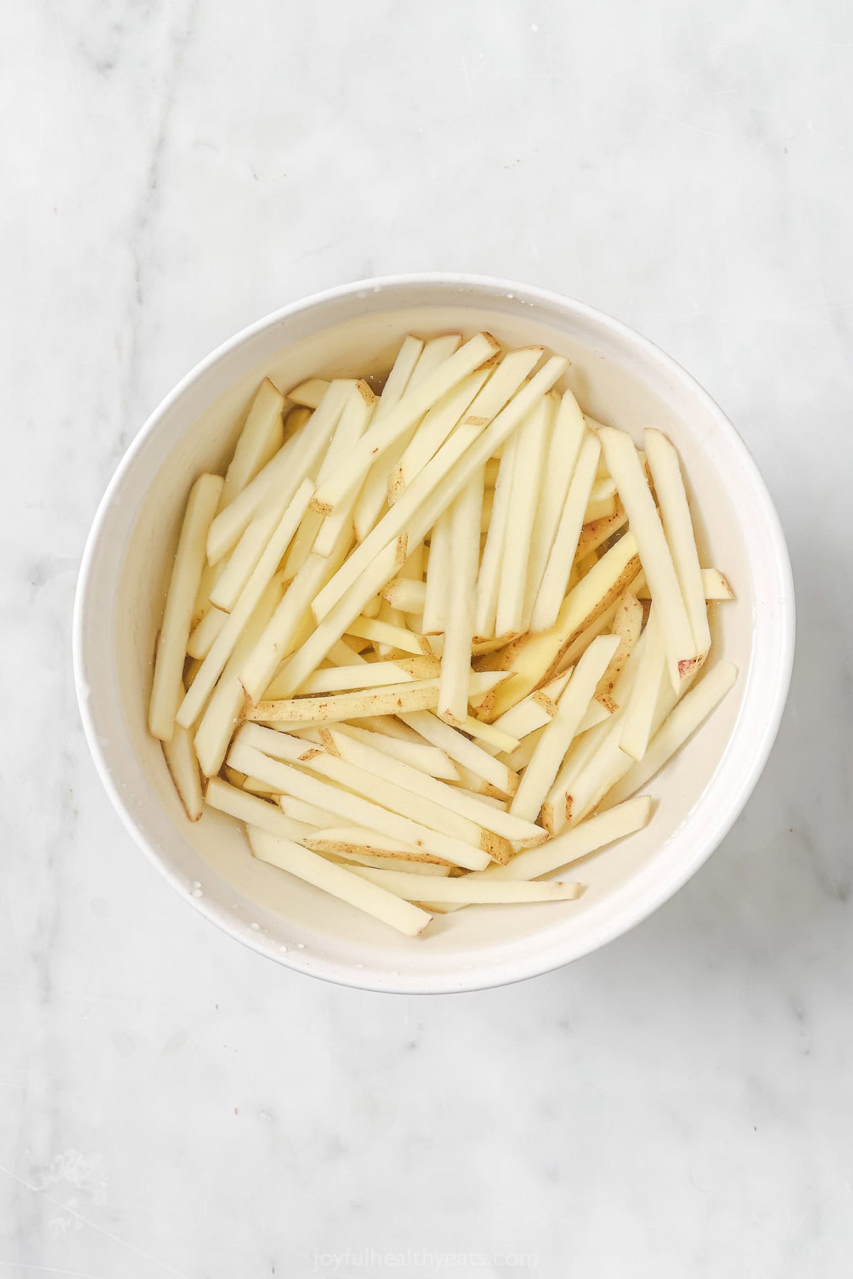 Cheesy Parmesan Truffle Fries are the perfect snack or party app when you’re feeling a little fancy. Baked in the oven and super crispy! Raw fries soaking in bowl of water