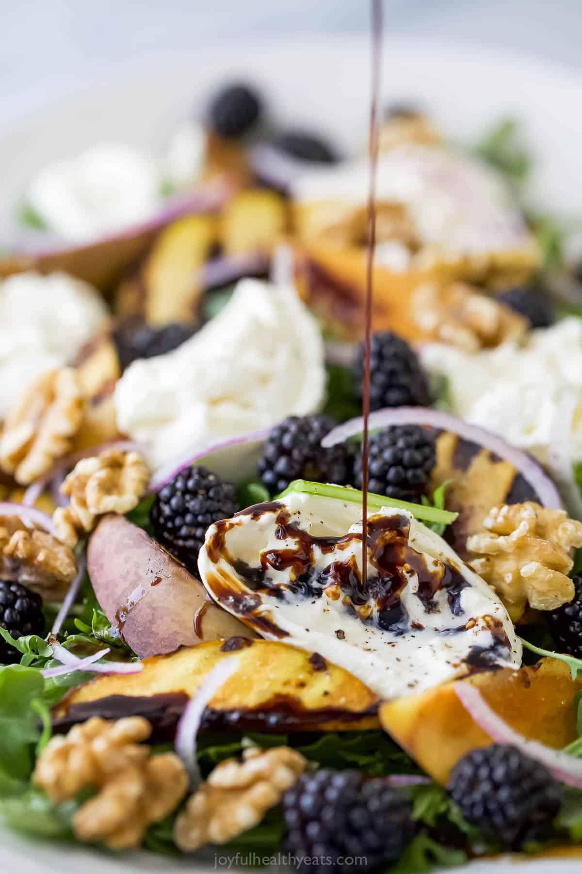 Drizzling balsamic vinegar onto burrata and grilled peach salad