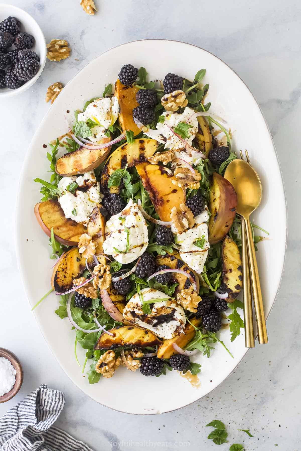 Overhead view of burrata and grilled peach salad on platter with fork and spoon