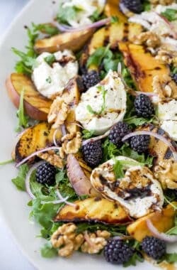 Platter with burrata and grilled peach salad, topped with blackberries, walnuts, and balsamic vinegar