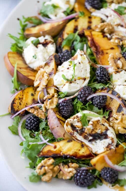 Platter with burrata and grilled peach salad, topped with blackberries, walnuts, and balsamic vinegar
