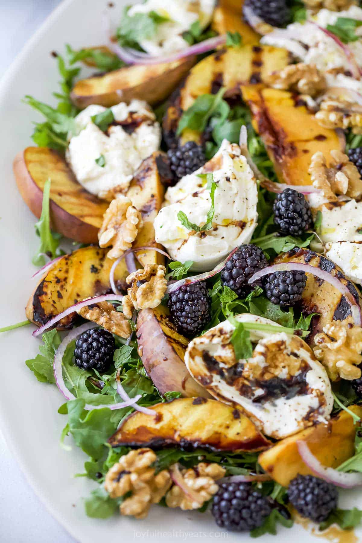 Platter with burrata and grilled peach salad, topped with blackberries, walnuts, and balsamic vinegar