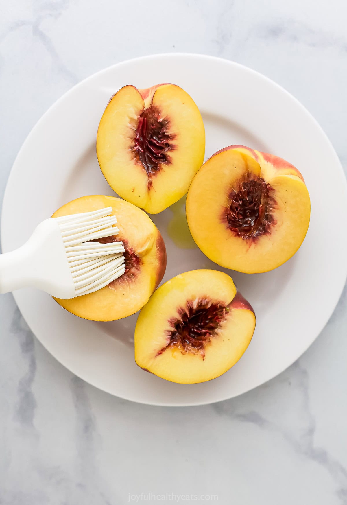 Brushing olive oil on cut sides of halved peaches