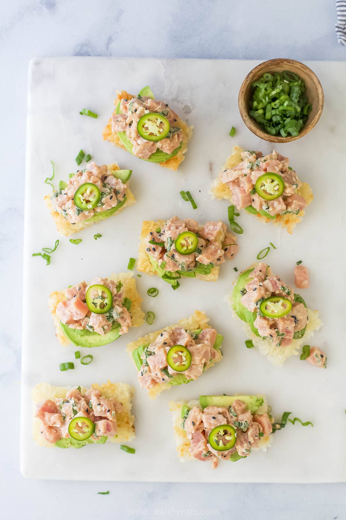 This Spicy Tuna Crispy Rice is a Nobu copycat that’s sure to impress! It’s easy to make, with ahi tuna topping crispy cubes of sushi rice. Overhead view of spicy tuna crispy rice bites on board