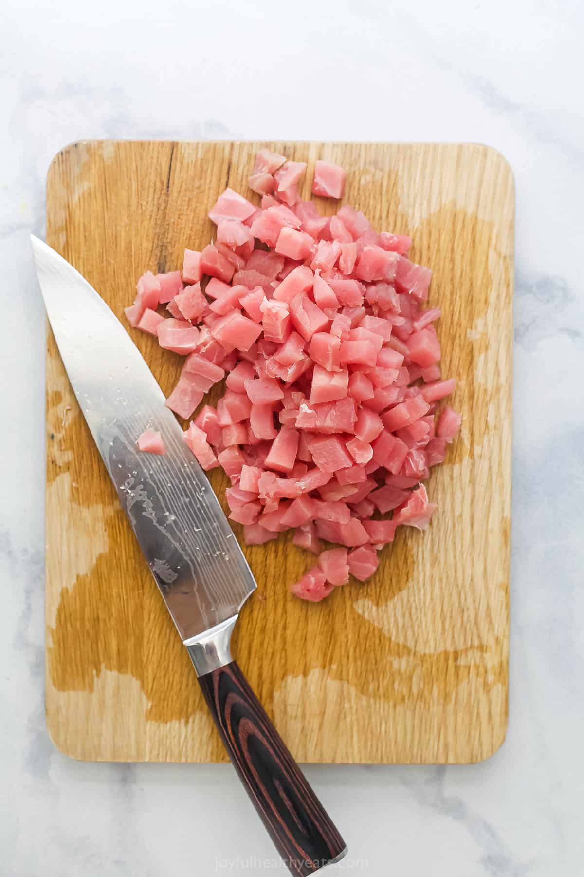 Overhead view of diced tuna on cutting board with chef's knife
