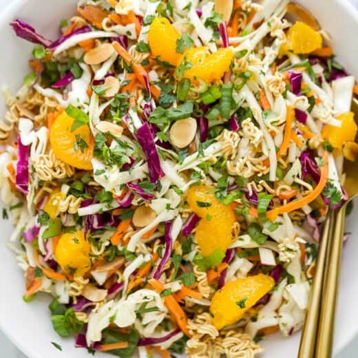 Overhead view of ramen noodle salad in white bowl with two gold spoons