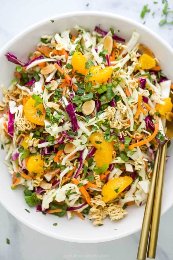Overhead view of ramen noodle salad in white bowl with two gold spoons