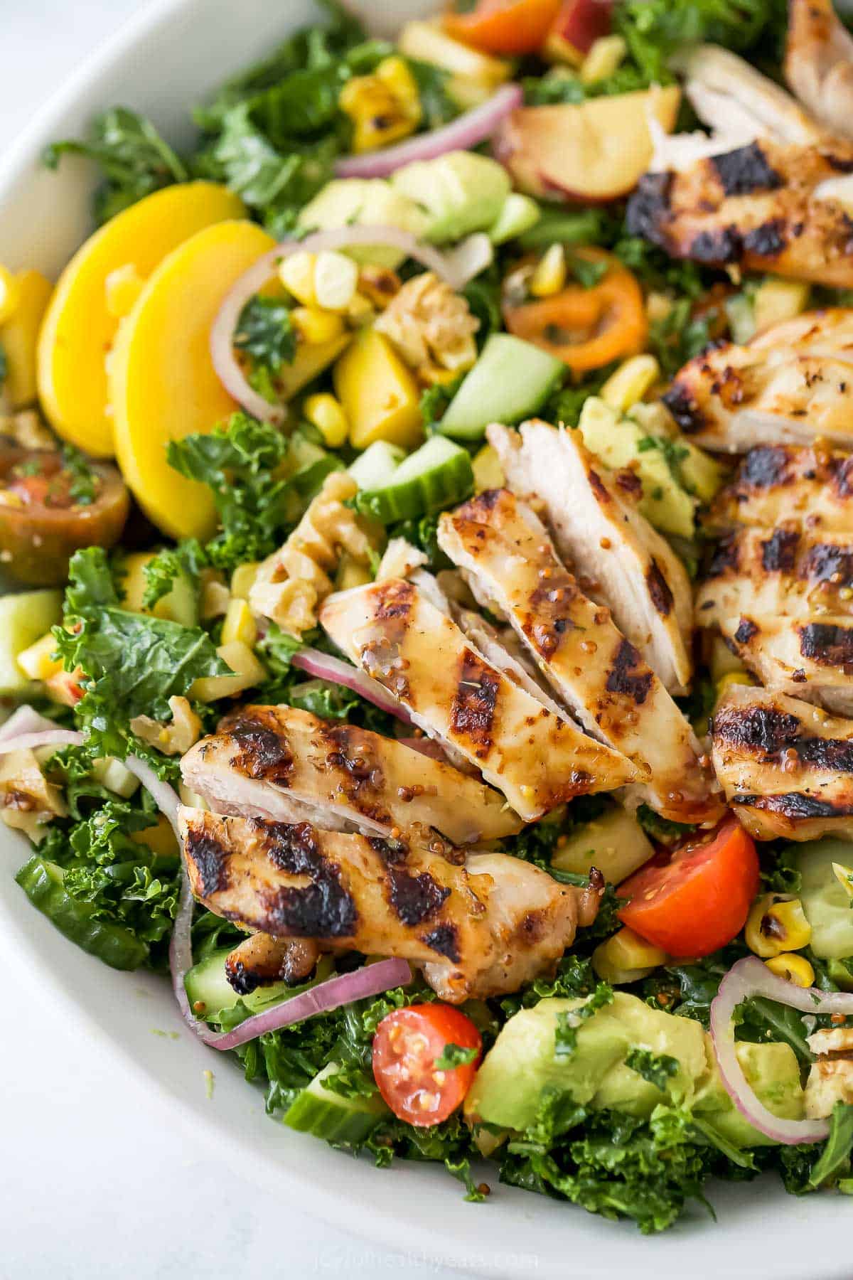 With sweet corn, peaches, tomatoes, grilled chicken and honey mustard dressing, this summer salad recipe is the perfect patio dinner! Sliced grilled chicken thighs served over summer salad recipe in bowl