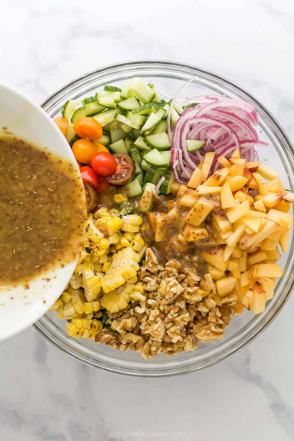 With sweet corn, peaches, tomatoes, grilled chicken and honey mustard dressing, this summer salad recipe is the perfect patio dinner! Pouring dressing into bowl of ingredients for summer salad recipe